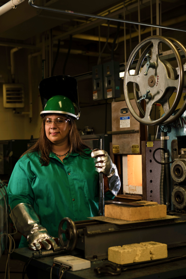 Laura Bartlett working at a lathe machine wearing green safety gear